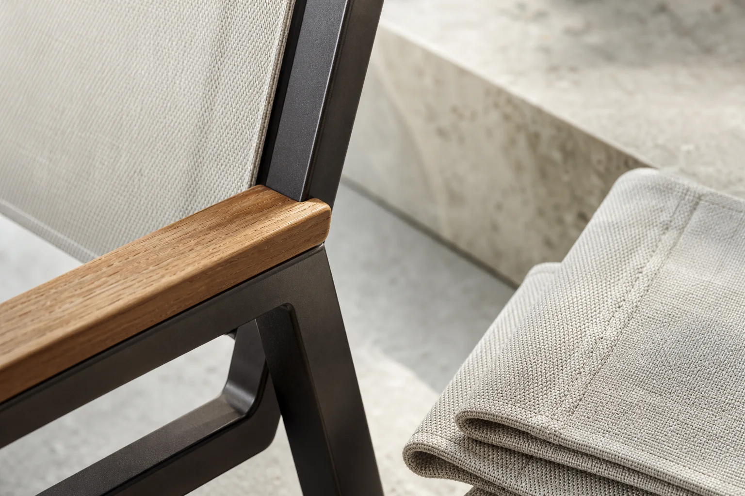 Nahaufnahme der Konstruktion: Travertinkante, Teak-Armlehne, Metallrahmen und Outdoor-Textil