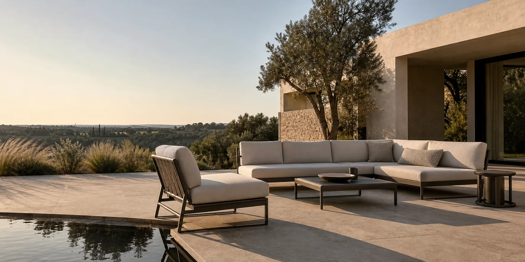 Weite Poolterrasse vor einem modernen Steinhaus mit Blick über eine mediterrane Hügellandschaft im Abendlicht